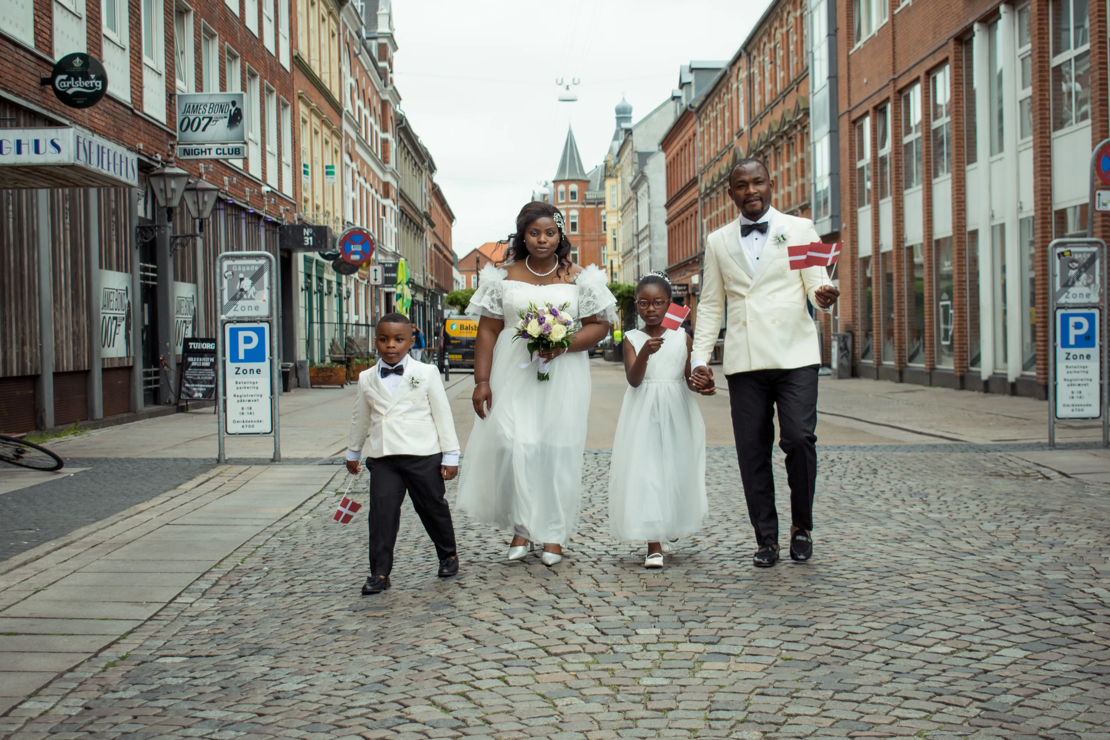 Ein dunkelhäutiges Paar, festlich für eine Hohzeit gekleidet. mit 2 Kindern kommt aus der Fußgängerzone einer typisch dänischen Stadt
