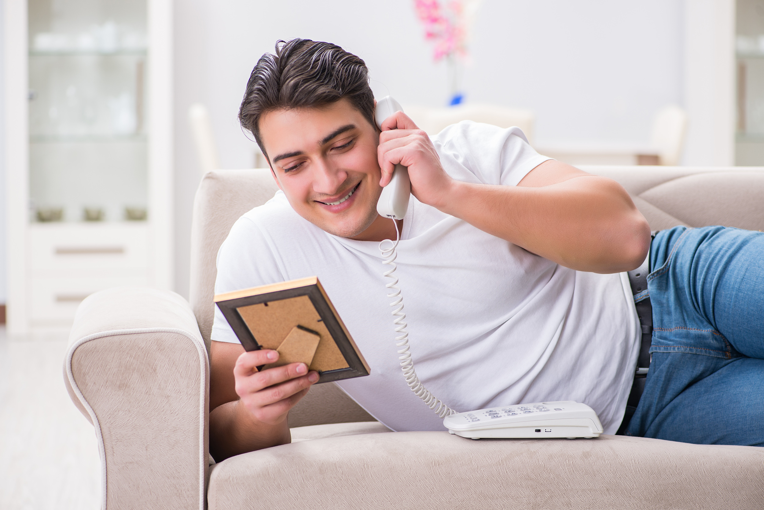 Mann liegt auf der Couch und telefoniert und schaut dabe ein Bild an.